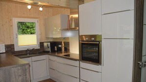 A modern kitchen with white cabinets, a built-in oven, and a window with blinds.
