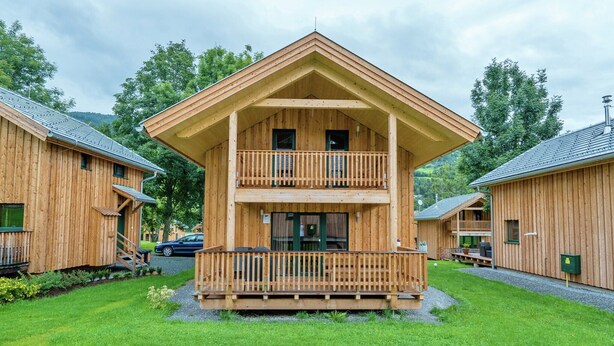A two-story wooden cabin with a balcony, surrounded by a well-maintained lawn and trees. - Spacious chalet with infrared sauna (Sankt Georgen am Kresichberg)