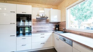 A modern kitchen with white cabinets, stainless steel appliances, and a wooden ceiling. - Spacious chalet with infrared sauna (Sankt Georgen am Kresichberg)