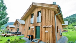 A wooden cabin with a deck, a green door, and a small outdoor seating area. - Spacious chalet with infrared sauna (Sankt Georgen am Kresichberg)