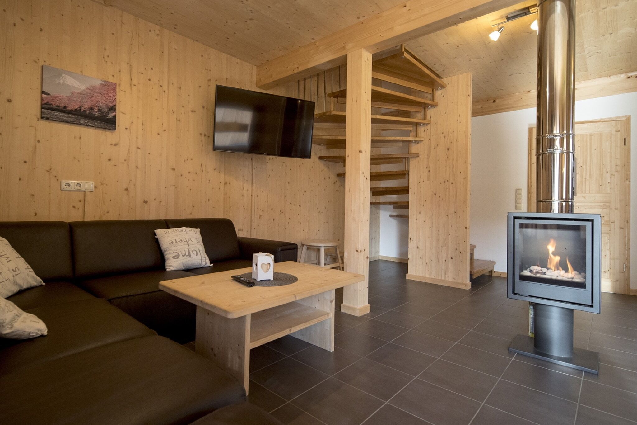 Interior em madeira com sofá, mesa, lareira e televisão na parede.