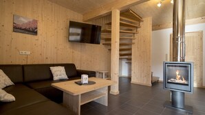 A wooden interior with a sofa, a table, a fireplace, and a TV mounted on the wall. - Spacious chalet with infrared sauna (Sankt Georgen am Kresichberg)