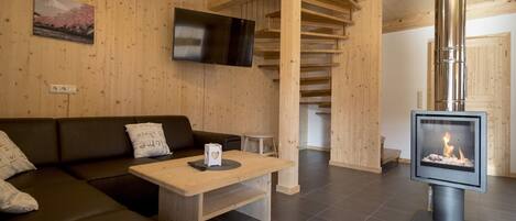 Un interior de madera con un sofá, una mesa, una chimenea y un televisor montado en la pared.