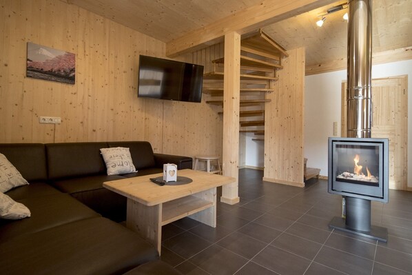 Un interior de madera con un sofá, una mesa, una chimenea y un televisor montado en la pared.