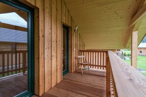 Una terraza de madera con puerta de vidrio que da a una habitación, una silla y una pequeña mesa.