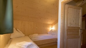 Een houten kamer met twee bedden, een deur en een wandlamp.