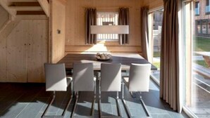 Un intérieur moderne avec un coin repas comprenant une table et des chaises en bois, de grandes fenêtres avec des rideaux et un escalier situé à gauche.