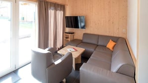 Un salon moderne avec un canapé gris, une petite table et un téléviseur fixé au mur.