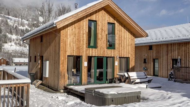 Une cabane en bois dotée d’un toit en pente, de grandes fenêtres et d’un espace extérieur aménagé avec des sièges.