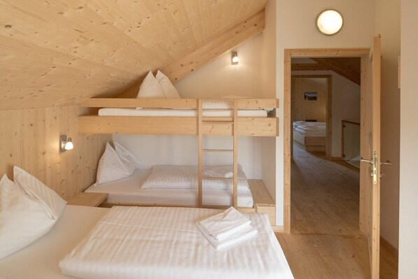 Quarto com beliches, teto de madeira e porta que dá para outro cômodo.