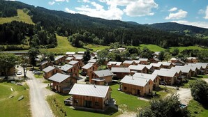 Un ensemble de chalets en bois aux toits inclinés, disposés de manière compacte, entourés de prairies verdoyantes et de collines boisées.