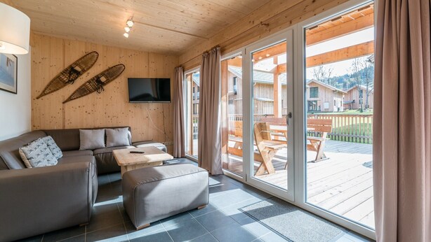 Un salon moderne avec un canapé, un pouf et un téléviseur à écran plat fixé au mur.