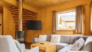 Un interior de cabaña acogedor, con paredes de madera, chimenea, sofá y televisor.