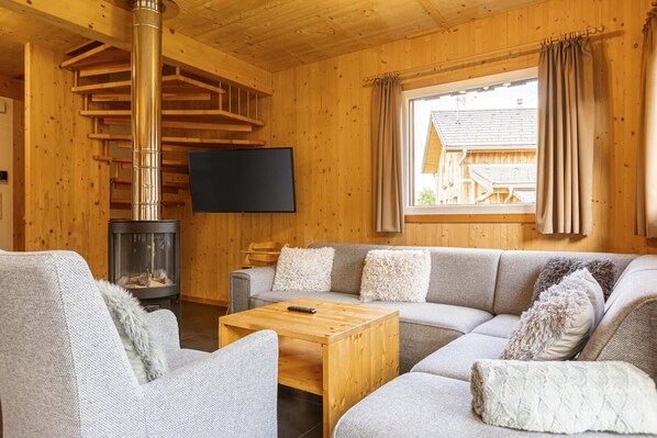 Un intérieur de chalet chaleureux, avec un revêtement mural en bois, une cheminée, un canapé et un téléviseur.