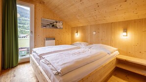 Habitación de cabaña de madera con dos camas, una ventana con cortinas, un cuadro en la pared y un pequeño calentador.