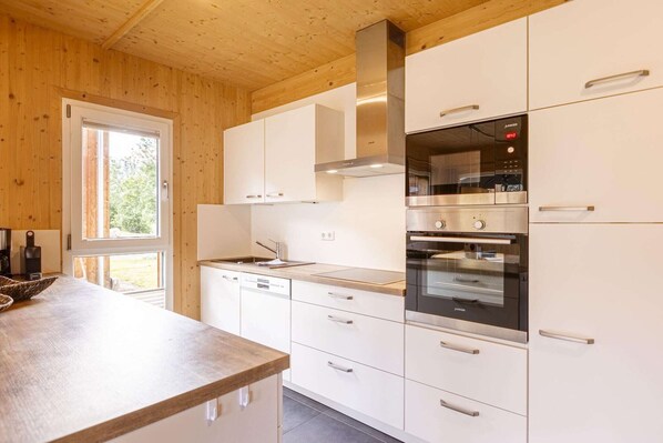 Una cocina moderna con armarios blancos, electrodomésticos de acero inoxidable y techo de madera.