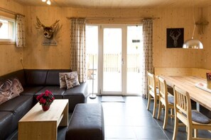 A cozy room with a wooden interior, a sofa, a dining table with chairs, and a large window with curtains.