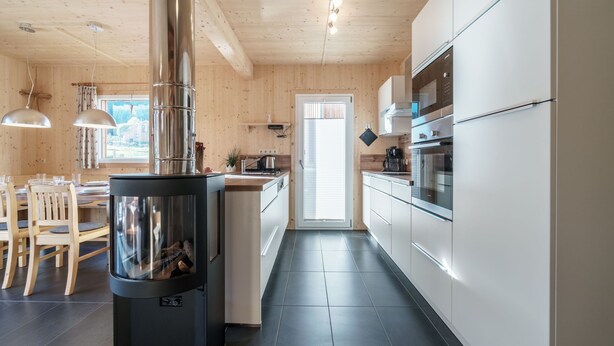 A modern kitchen with wooden walls, a central stove, white cabinets, and a dining area with wooden chairs.