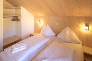 Une chambre avec deux lits, des murs en bois et une étagère où sont pliées des serviettes.