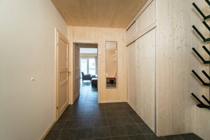 Um corredor com paredes de madeira e chão de azulejos, que leva a um quarto com espelho e uma cadeira.