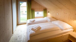 A wooden cabin bedroom with two beds, a window with curtains, and a view of the outside.