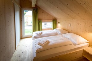 Quarto de cabana de madeira com duas camas, janela com cortinas e vista para o exterior.