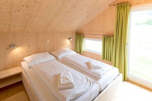 Une chambre dans une cabane en bois, avec deux lits, une fenêtre avec des rideaux et une table de chevet.
