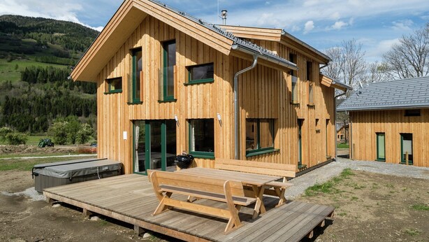 A wooden cabin with a deck, a covered outdoor seating area, and a view of the surrounding landscape.