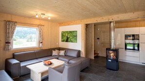 A modern interior with a wooden ceiling, a large sofa, a coffee table, a fireplace, and a kitchen area.