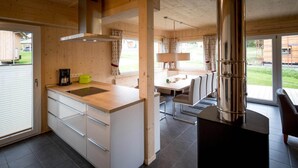 A modern kitchen with a central island, a dining area with a table and chairs, and a large window providing a view of the outdoors.