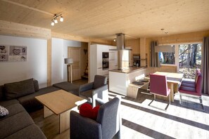 A modern, open-plan living area with a sofa, chairs, a dining table, and a kitchen. - Charming chalet with whirlpool (Sankt Georgen am Kresichberg)