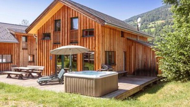 En stuga byggd av trä med ett bubbelbad, picknickbord och en veranda.