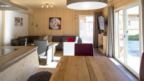 En modern inredning med ett träpanelat tak, en matplats, en soffgrupp, en tv och utsikt över omgivningen.