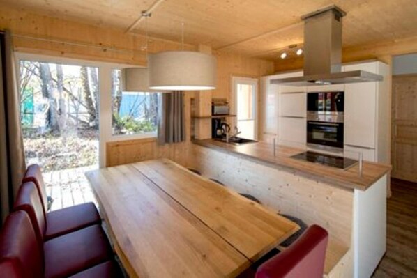 A modern kitchen with wooden cabinetry, a central island, and a dining area with red chairs. - Charming chalet with whirlpool (Sankt Georgen am Kresichberg)