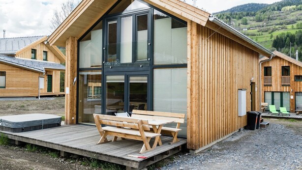 Una cabaña de madera con un amplio ventanal y una terraza de madera con un banco.