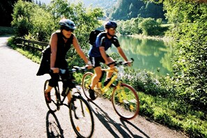 Dos ciclistas en un camino pavimentado junto a un lago, rodeados de vegetación.