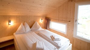 Une chambre dans un chalet en bois, avec deux lits, deux lampes fixées au mur et une fenêtre.