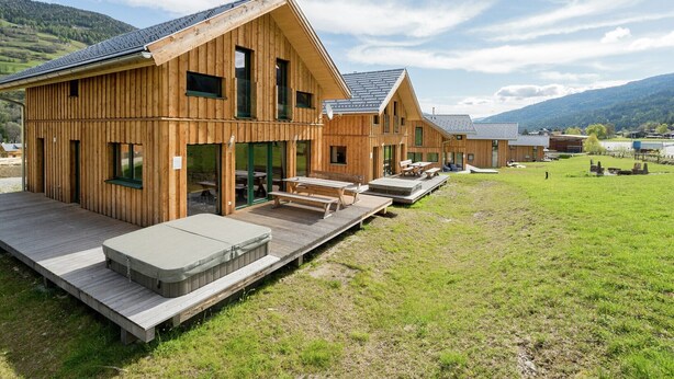 Une rangée de cabanes en bois, dotées d’espaces extérieurs aménagés pour s’asseoir, et un champ verdoyant en arrière-plan.