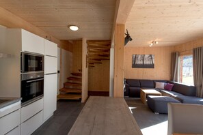 A modern kitchen with built-in appliances, a wooden staircase, a living area with a sofa and coffee table, and a large window.