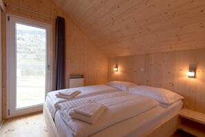Et hyggeligt sommerhusværelse med to senge, et vindue med gardiner og vægmonterede lamper.