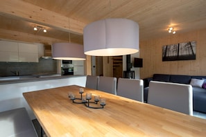 A modern kitchen with wooden cabinets, a dining table with candles, and a living area with a sofa and a painting on the wall.