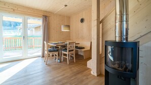 A wooden interior with a dining area, a fireplace, and a large window with a view of a wooden deck and mountains.