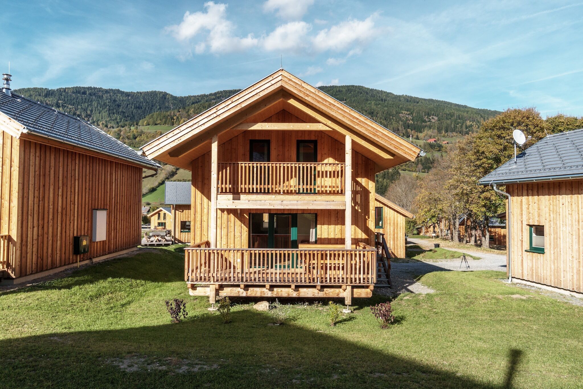 Eine Holzchalet mit Balkon, umgeben von einer üppigen grünen Landschaft und Bergen im Hintergrund.