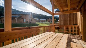 A wooden deck with a view of rustic buildings and a grassy field.