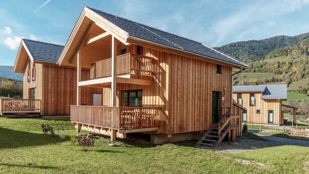 A wooden chalet with a balcony, a staircase, and a view of the surrounding landscape.