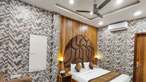 A bedroom with a large bed, wooden headboard, two bedside tables, a ceiling fan, and patterned wallpaper. - Hotel The Restu (Amritsar)