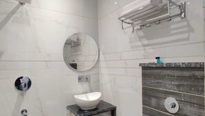 A modern bathroom with a white sink, a round mirror, a towel rack, and a toilet. - Hotel The Restu (Amritsar)