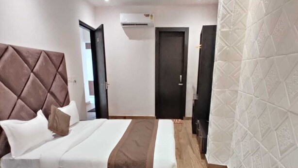 A hotel room with a large bed, a ceiling fan, an air conditioning unit, and a wooden floor. - Hotel The Restu (Amritsar)