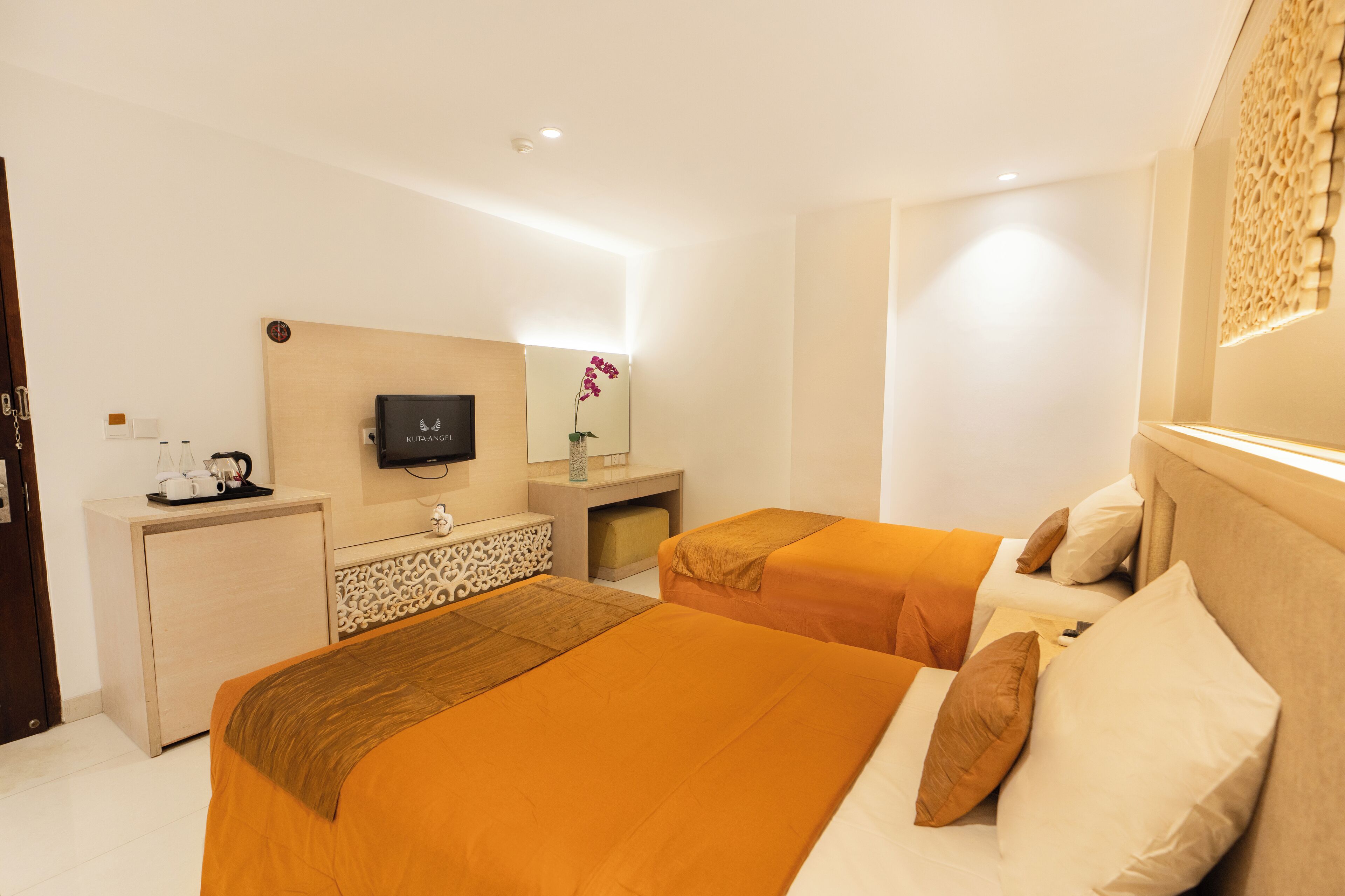 A hotel room with two beds, a desk, a television, and a decorative wall piece.