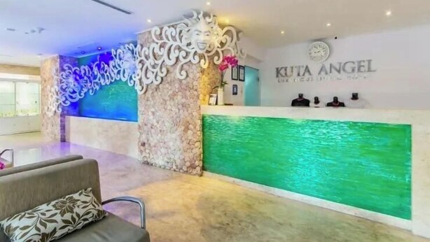A reception area with a stone pillar, a reception desk, and a green water feature. - Kuta Angel Hotel (Kuta)